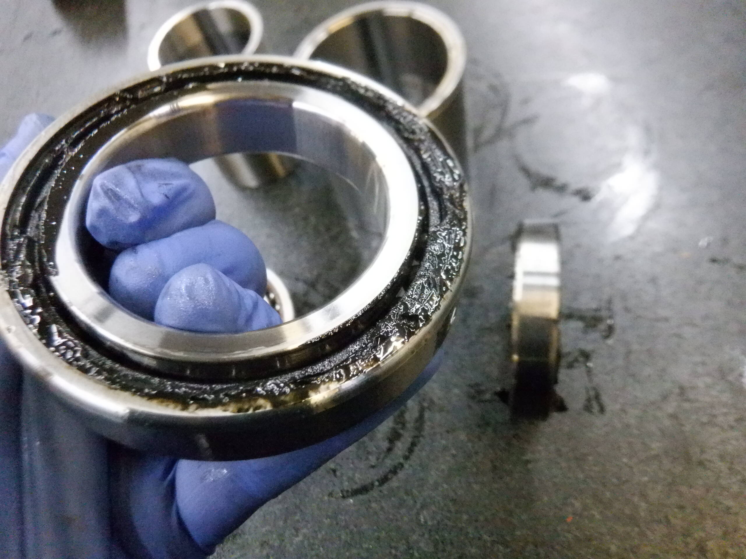 A worn ball bearing held in a gloved hand shows internal damage and deterioration.